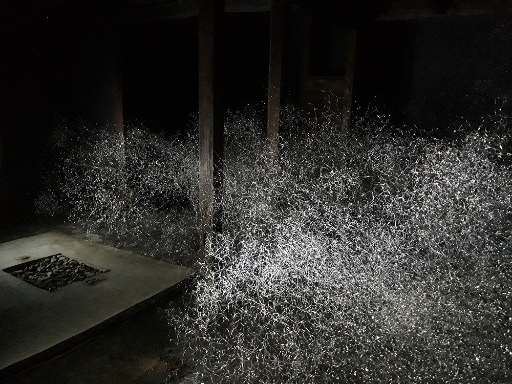 A cloud of silvery material hangs in a dark stone room with wooden pillars.