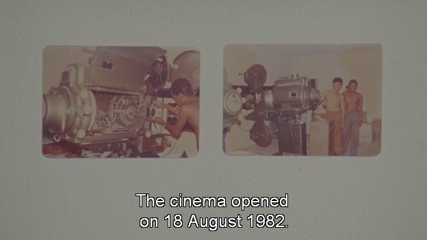 Two photographs sit on a grey background. The left one shows someone working on a large, metal film projector. The right one shows several people standing next to the now assembled projector. Subtitles at the bottom read: 'The cinema opened on 18 August 1982.