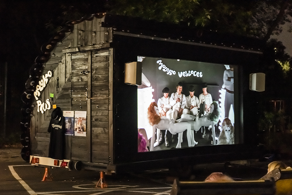 A carriage converted to hold a cinema screen showing a scene from Clockwork Orange at night.