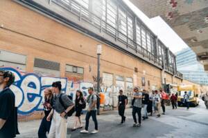 A line of people walking down a street. Some are mid-conversation.