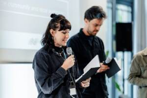 Heather Bradshaw presenting her group's project pitch. A man stands beside her holding a notebook