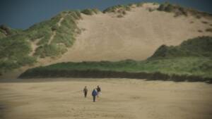 Still from The Son and the Sea. In the far distance, three men are walking through a sandy landscape.