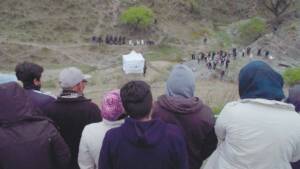 Still from LANDMARKS of a crowd of people on a fill, looking down at a white tent and other people walking around in the valley below.