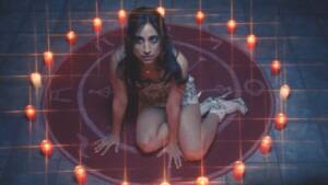 Still from FUCKTOYS of a woman sitting in the centre of a pentagram, surrounded by candles. She looks afraid and wears a short dress and high heels.