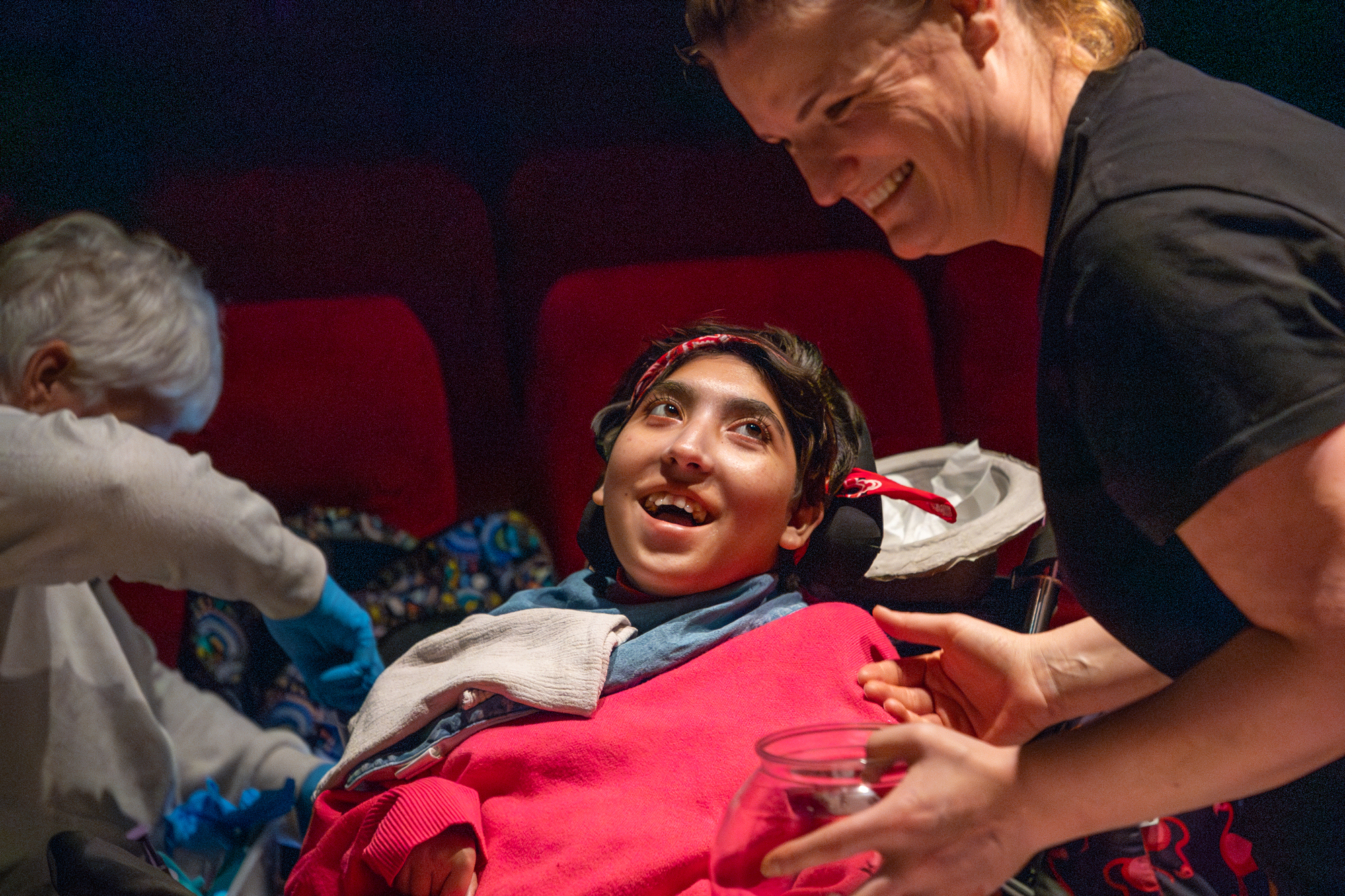 An audience member in a cinema looks up a member of Front of House who is holding a bowl. Both are smiling broadly.